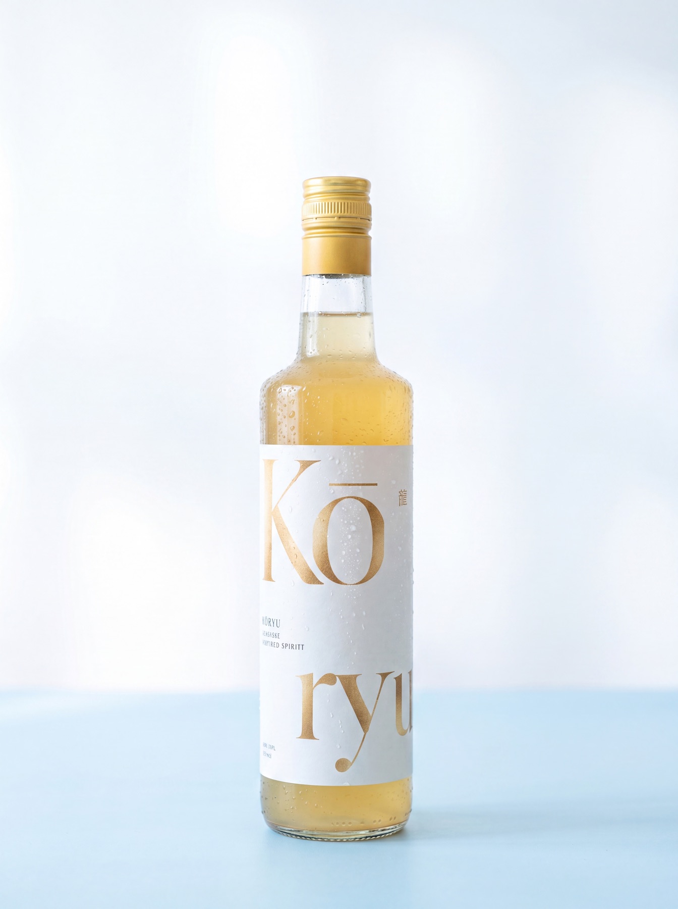 A 700 ml bottle of Kōryu, pale golden spirit behind a cream label with gold lettering, on a soft studio backdrop.