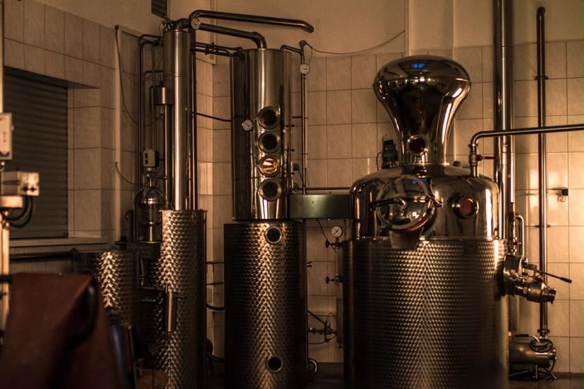 Copper and stainless steel pot stills at a small artisan distillery, warmly lit against white tiled walls.